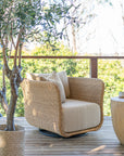 Malusi one seater outdoor lounge chair with natural rattan weave and cushioned seat, styled on a timber deck beside an olive tree and timber side table.