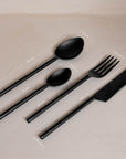 A sophisticated matte black cutlery set featuring a modern fork, knife, tablespoon, and teaspoon with sleek, contemporary handles