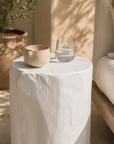 White magnesium oxide Meera stool styled beside an outdoor lounge creating a light and tranquil setting with soft textures and natural Mediterranean inspired warmth.