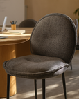 Dark grey upholstered Mhaya Chair with rounded backrest styled at a modern timber office table with soft natural light.