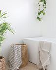 A bright, modern bathroom featuring a woven storage basket, a freestanding bathtub, and soft striped towels, creating a spa-like retreat with natural textures