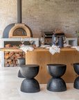 Outdoor entertaining area featuring sculptural black stools, woodfire pizza oven, and oak island bench styled for dining.