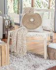 Light-filled modern boho livingroom with layered neutral throws, woven accent chair with white rope weave, natural wood side tables, and organic decor accents.