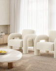 A pair of modern boucle armchairs with sculptural rounded arms, upholstered in soft white fabric, styled in a serene contemporary lounge setting with natural tones