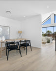 Modern Scandinavian dining room with natural wood table and black woven rope armchairs, featuring floor-to-ceiling windows and minimalist decor