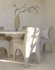 Modern dining room with a sculptural travertine table, textured upholstered chairs, and a handcrafted paper mâché vase, creating a serene and elegant space