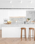 A bright modern kitchen featuring Kulala Living solid oak bar stools with black metal footrests. Styled with a marble benchtop, white cabinetry, and natural wood accents for a contemporary coastal aesthetic