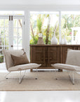 Contemporary lounge space featuring neutral linen chairs with metal legs, a rustic wooden sideboard, white ceramic vases, and a textured jute rug, creating a serene, nature-inspired aesthetic.