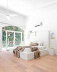 Bright and airy minimalist bedroom with a white plaster bed, soft natural-toned bedding, and large arched windows offering lush green outdoor views, creating a tranquil retreat