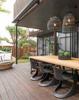 Modern outdoor dining area with black woven pendant lights, timber table, sleek black chairs, and natural landscaping