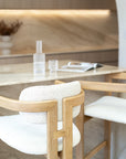 Rubberwood counter-height chair with curved frame and ivory boucle upholstery, styled at a travertine kitchen island with soft neutral tones and minimal decor.