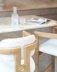 Rubberwood counter-height chair with curved frame and ivory boucle upholstery, styled at a travertine kitchen island with soft neutral tones and minimal decor.