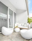Modern outdoor balcony seating with white curved armchairs, natural rope sofa with white cushions, and a minimalist round side table.