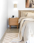 Oak Molly bedside table styled with neutral decor beside a linen-draped bed in a calm, contemporary bedroom setting