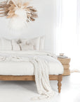 KULALA Living Mon Bed with turned timber legs, styled with white linen bedding and sculptural neutral-toned decor in a bright, serene bedroom