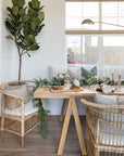 A beautifully styled dining space featuring natural rattan dining chairs, a solid timber table, and an elegant table ascape with candles and greenery, creating a warm and inviting atmosphere