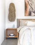 Oak Bedside Table styled in a modern neutral bedroom with soft linen bedding, woven pendant light and art detail.