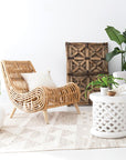 A beautifully handwoven natural rattan lounge chair with an organic silhouette and sturdy wooden legs. Styled in a bright, airy living space with neutral textures and lush greenery, creating a relaxed and inviting atmosphere
