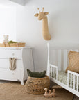 A serene nursery setting featuring woven storage baskets, a white wooden cot, a matching dresser, and a macrame hanging planter, creating a warm and natural space for a baby