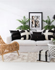 A handwoven natural rattan lounge chair with a sculptural design, styled in a contemporary living space featuring a white linen sofa, black-and-white geometric cushions, and lush green ferns. The setting blends modern and organic textures for a relaxed yet sophisticated aesthetic