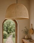 Natural rattan dome pendant light hanging in a soft-toned interior entryway with timber accents and arched door opening to a garden path