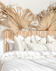 Natural teak wood panel bedhead styled with textured linen bedding and decorative palm leaves. Warm, earthy tones create a serene and inviting bedroom space, blending organic materials with relaxed coastal aesthetics.