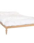 Natural wood platform bed with turned legs styled with white linen bedding and textured throw