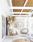 Outdoor lounge setting featuring natural woven lounge chairs with white metal frames, paired with white cushions and decorative round pillows. Styled with a large ceramic vase and dried pampas arrangement under a pergola with bamboo ceiling. Relaxed, coastal vibe perfect for outdoor living.
