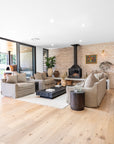 A beautifully styled lounge featuring neutral linen sofas, a black timber coffee table, and a fireplace set against a rustic brick wall. The space is enhanced with natural textures, earthy décor, and warm timber flooring, creating a relaxed and inviting atmosphere