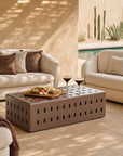 Niche Coffee Table in chocolate styled in an outdoor lounge setting with two curved cream sofas, neutral cushions, and a poolside backdrop.