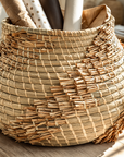 Handwoven Nokosi basket in natural fibres with layered textured detailing, styled with wrapping paper and warm sunlit coastal decor.