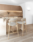 Pair of oak Nordic-style bar stools with upholstered seats at a marble kitchen island featuring curved timber cabinetry and integrated lighting.