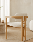 Contemporary dining chair with solid oak frame and curved cream boucle upholstered seat and backrest, styled in a soft neutral living space with timber floors