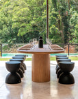 Elegant outdoor dining scene featuring a handcrafted teak table paired with black hourglass stools, overlooking lush greenery and a serene pool.