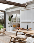 Rustic outdoor dining bench with a wooden table on a farmhouse-style deck, featuring grazing platter, wine glasses, and cozy decor