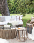 Tranquil outdoor lounge setting featuring the makena Chairs, a teak coffee table, and a cosy white-cushioned sofa styled with soft throws and textured cushions, set against a lush green garden backdrop