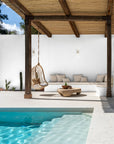 Outdoor setting with a rattan hanging chair, stone coffee table, and built-in lounge under a pergola beside a turquoise pool