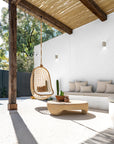 Outdoor setting with rattan hanging chair, low coffee table, built-in cushioned bench seating and pergola shade by the pool.