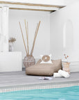 Sandy beige outdoor beanbag by the poolside, styled with a white decorative cushion, rustic wooden side table, and natural decor accents, creating a serene and stylish relaxation space.