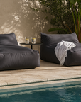 Pair of black Playa Pool Bean Bags beside a pool, styled with a throw, side table, and two glasses of water in a lush outdoor setting.