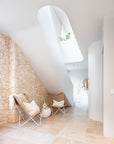 A pair of rattan sling chairs with white metal frames styled in a modern coastal interior, set against a natural stone wall with soft neutral décor for a relaxed and inviting aesthetic