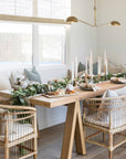 A beautifully styled dining space featuring natural rattan dining chairs, a solid timber table, and an elegant table scape with candles and greenery, creating a warm and inviting atmosphere