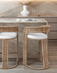 Close-up of a marble kitchen island styled with curved rattan barstools featuring white cushions, paired with soft lighting and earthy decor for a natural, relaxed look.