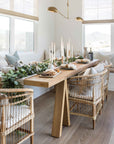 A beautifully styled dining space featuring natural rattan dining chairs, a solid timber table, and an elegant table scape with candles and greenery, creating a warm and inviting atmosphere