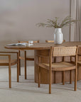Elegant round oak dining table paired with woven rattan chairs, creating a warm and inviting dining space with natural textures