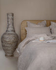 Rustic tall paper mache vase styled next to a modern timber bed with natural linen bedding, creating a serene bedroom aesthetic