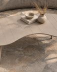 Solara coffee table with soft rounded top and tapered legs styled with ceramic vessels on a textured outdoor surface.