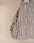 A generously sized striped linen market bag with a relaxed, slouchy design and exterior pocket. The neutral-toned fabric and soft texture create a timeless, effortless style