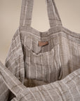 A generously sized striped linen market bag with a relaxed, slouchy design and exterior pocket. The neutral-toned fabric and soft texture create a timeless, effortless style