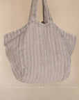 A generously sized striped linen market bag with a relaxed, slouchy design and exterior pocket. The neutral-toned fabric and soft texture create a timeless, effortless style
